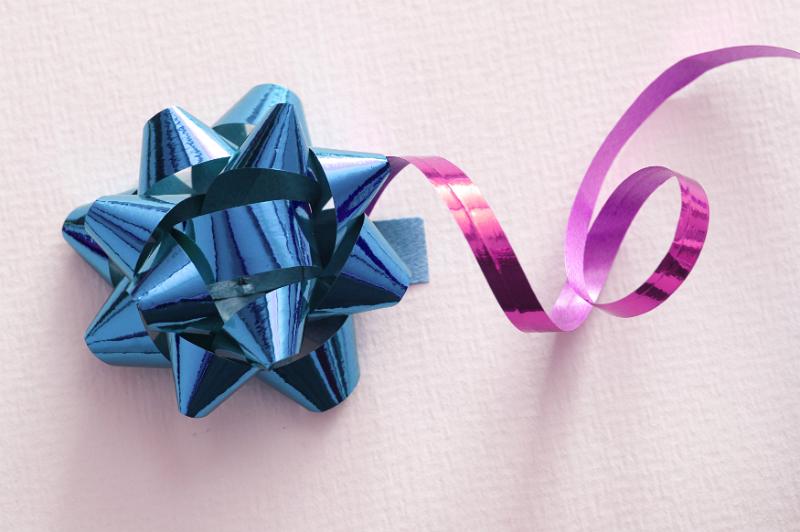 Free Stock Photo: Shiny blue foil bow with twirled pink ribbon for decorating the packaging of a gift over a white background with copy space